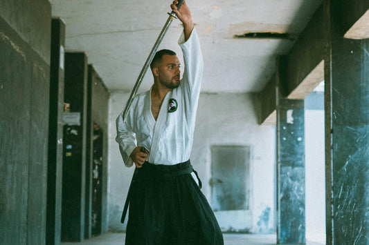 A man dressed in martial arts clothing practicing with a sharp katana.